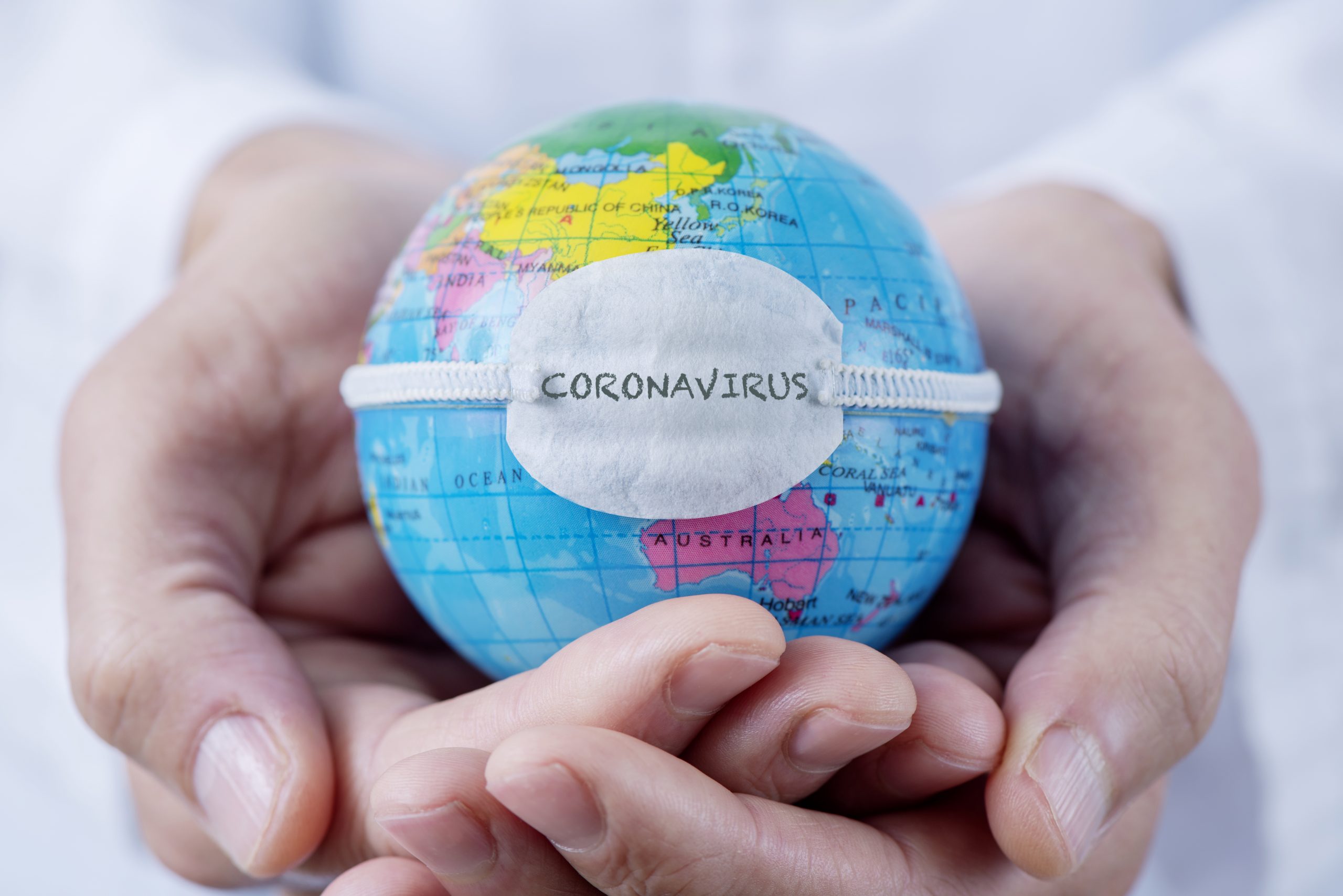 closeup of a doctor holding a world globe with a protective mask with the word coronavirus written in it