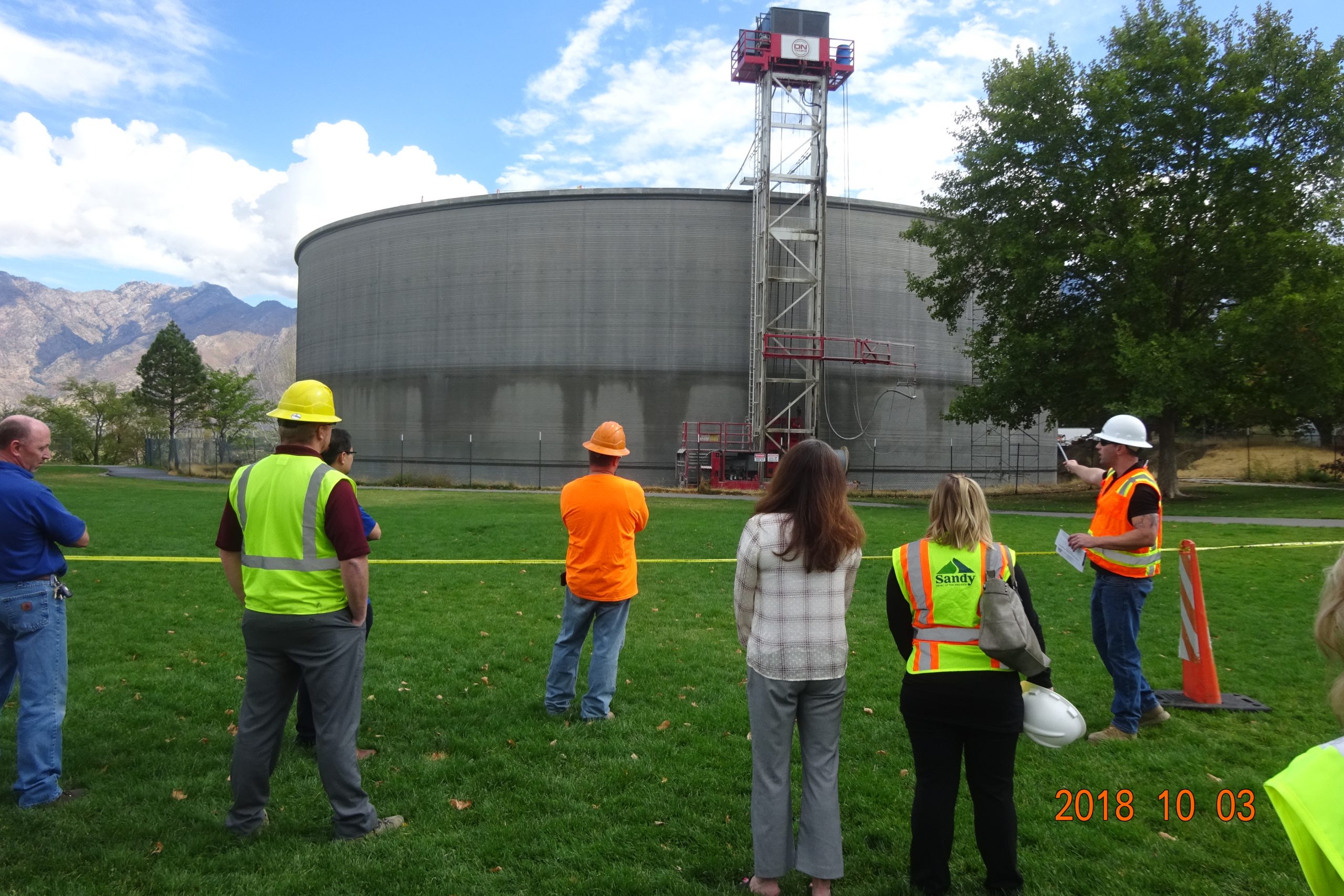 Construction workers standing on grass looking at concrete water tank in Sandy City.