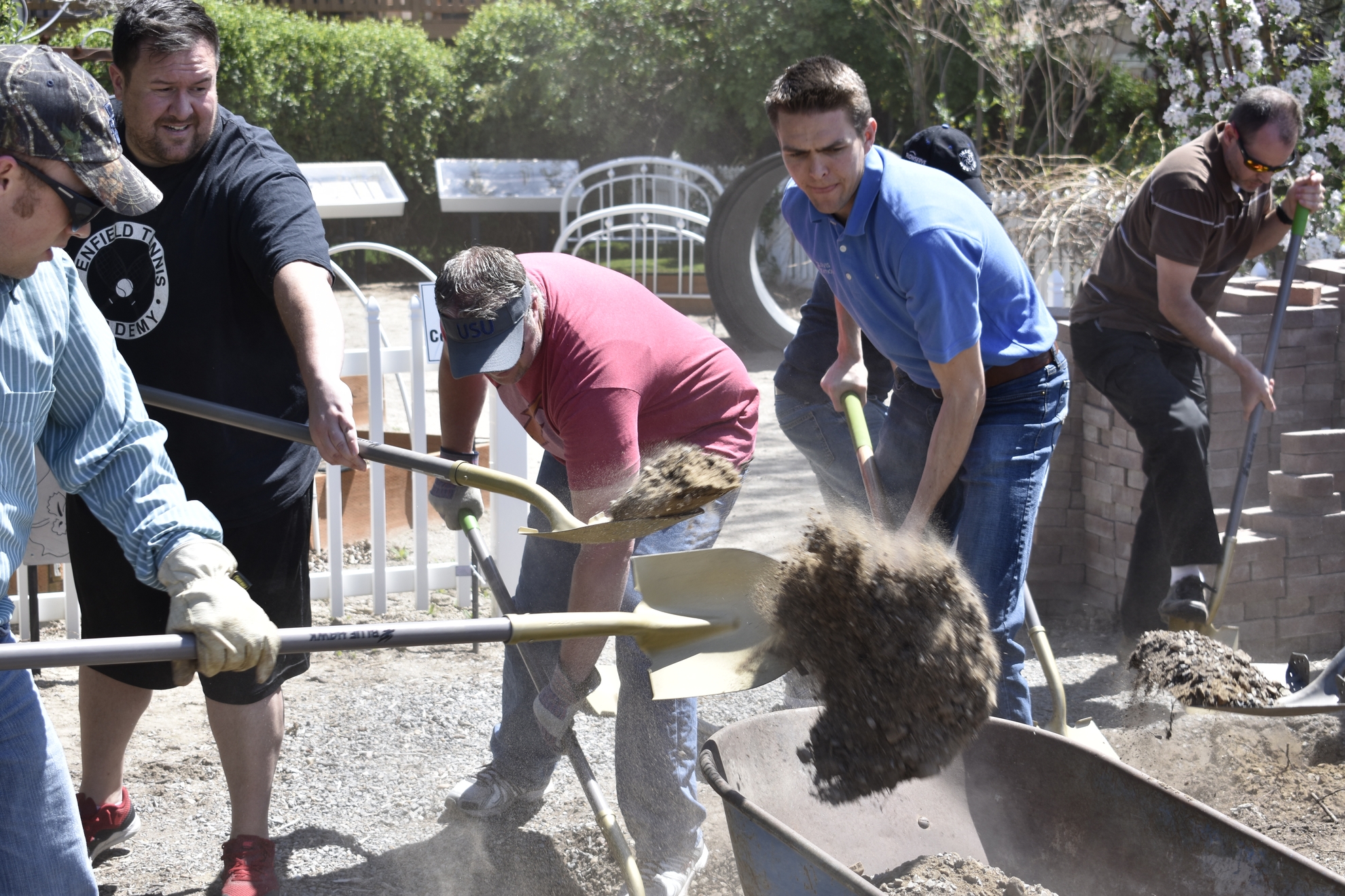 Group of men shoveling dirt into wheelbarrow. 