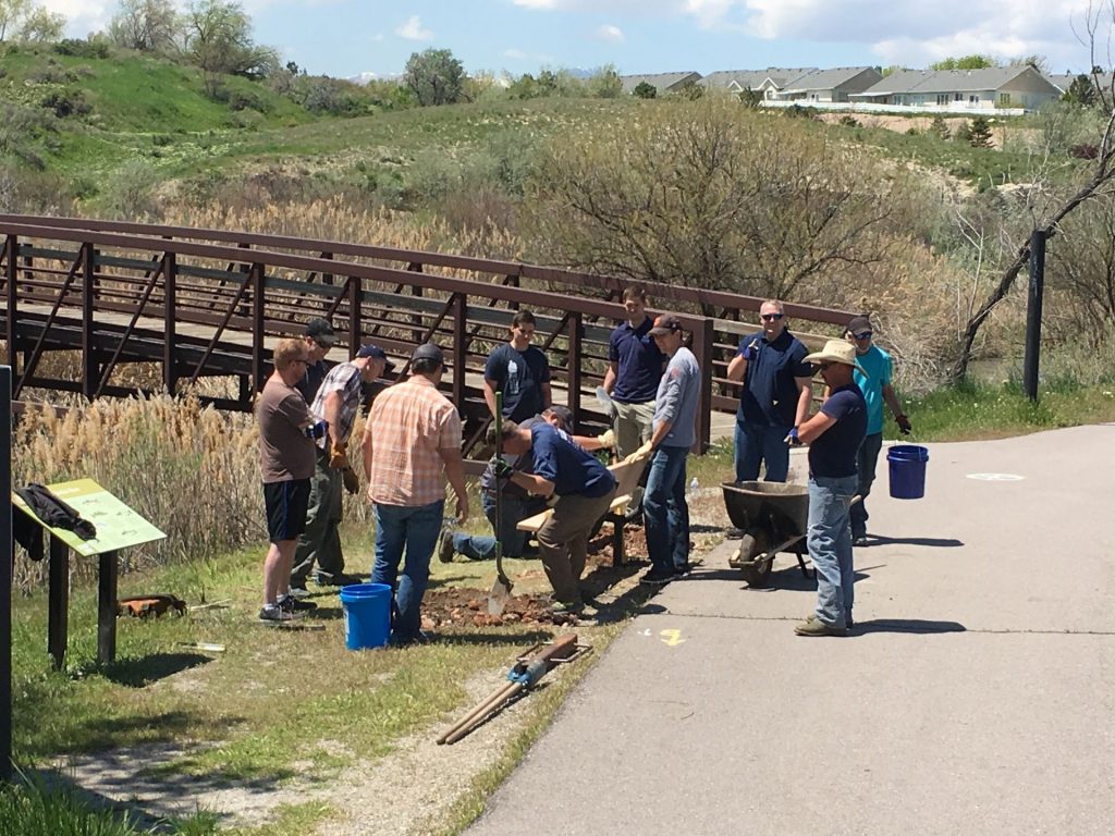 Men gathered around outside standing by a small bridge while digging holes.