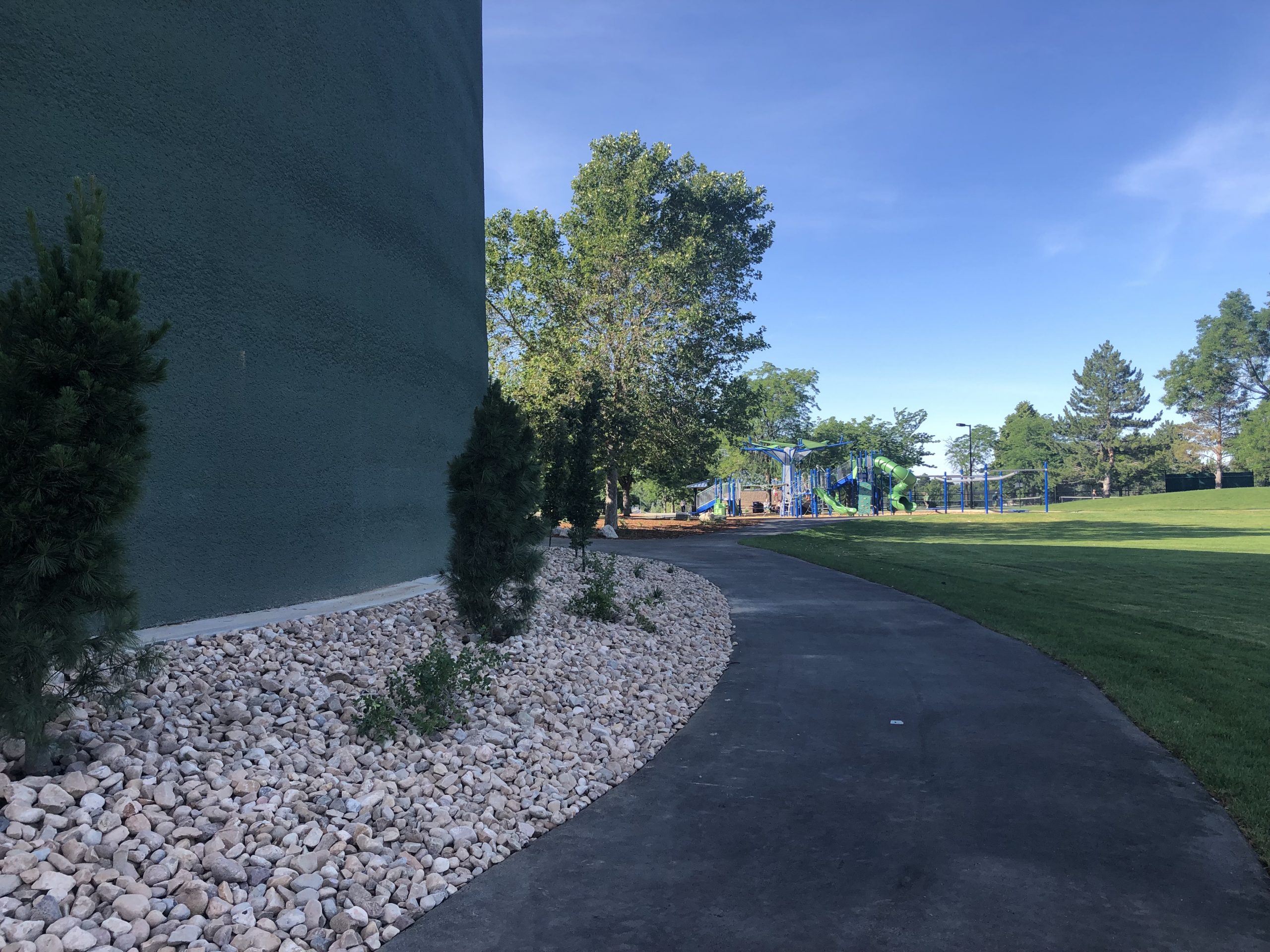 Sidewalk that goes around circular concrete tank beside park with grass and playground.