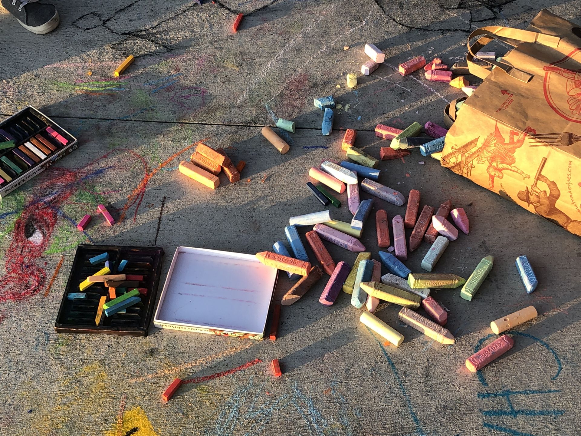 Sticks of sidewalk chalk laying on sidewalk amongst sidewalk drawings. 